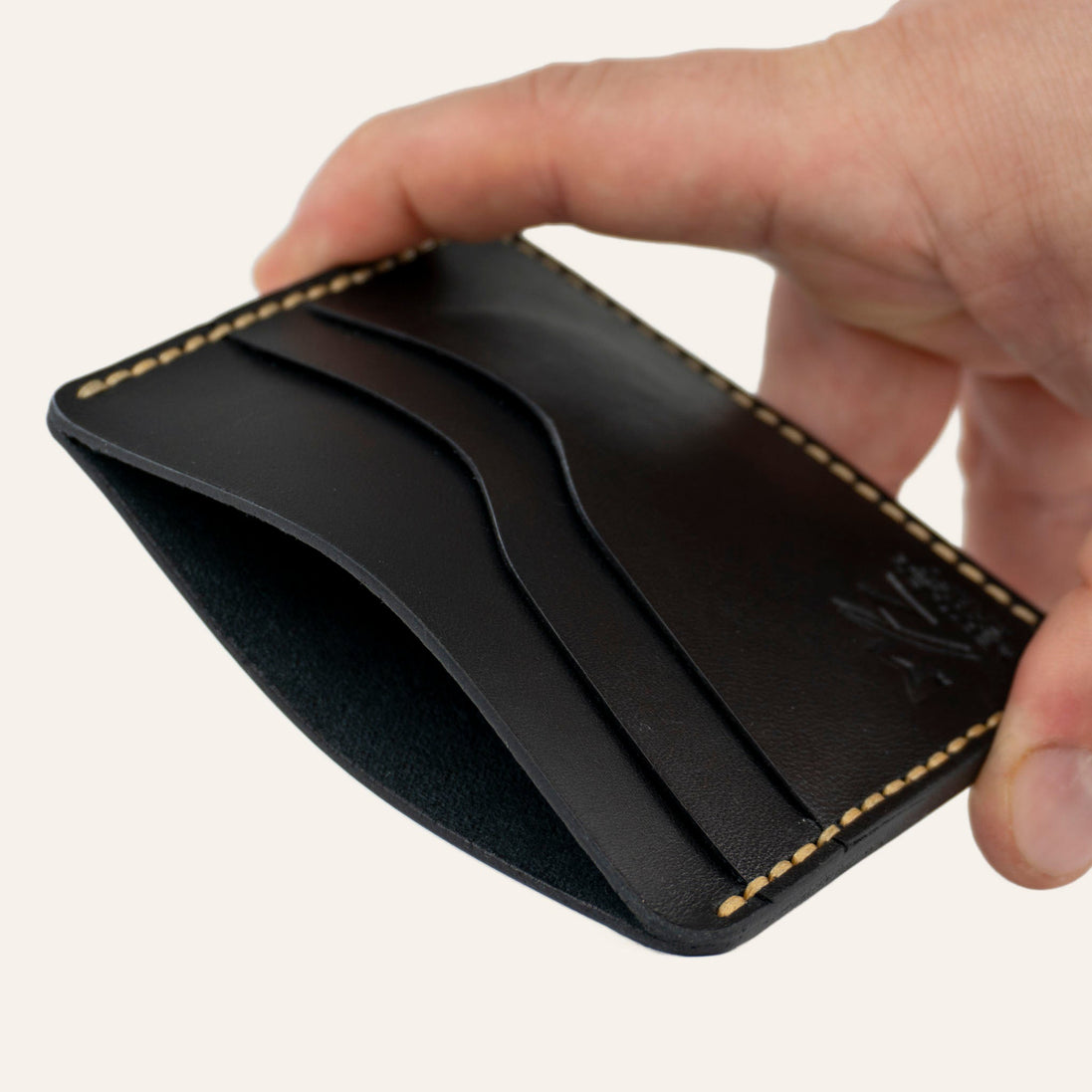 MZ Leather Craft yatay minimalist siyah Buttero deri kartlık, el ile tutulan hafif açılı boş ön görünüm, kıvrımlı kart yuvaları ve sarı saraç dikişi detayları