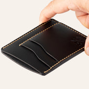 MZ Leather Craft dikey minimalist siyah Buttero deri kartlık, el ile tutulan hafif açılı boş ön görünüm, kıvrımlı kart yuvaları ve sarı saraç dikişi detayları