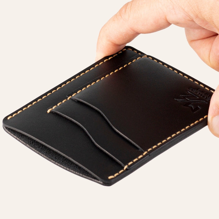 MZ Leather Craft dikey minimalist siyah Buttero deri kartlık, el ile tutulan hafif açılı boş ön görünüm, kıvrımlı kart yuvaları ve sarı saraç dikişi detayları