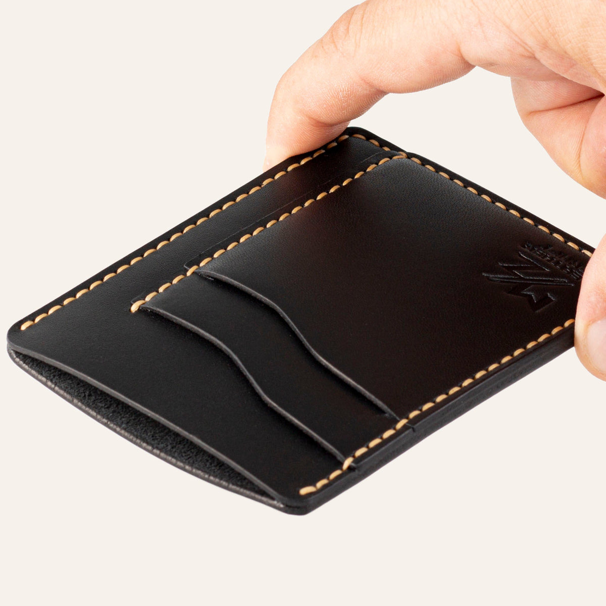MZ Leather Craft dikey minimalist siyah Buttero deri kartlık, el ile tutulan hafif açılı boş ön görünüm, kıvrımlı kart yuvaları ve sarı saraç dikişi detayları