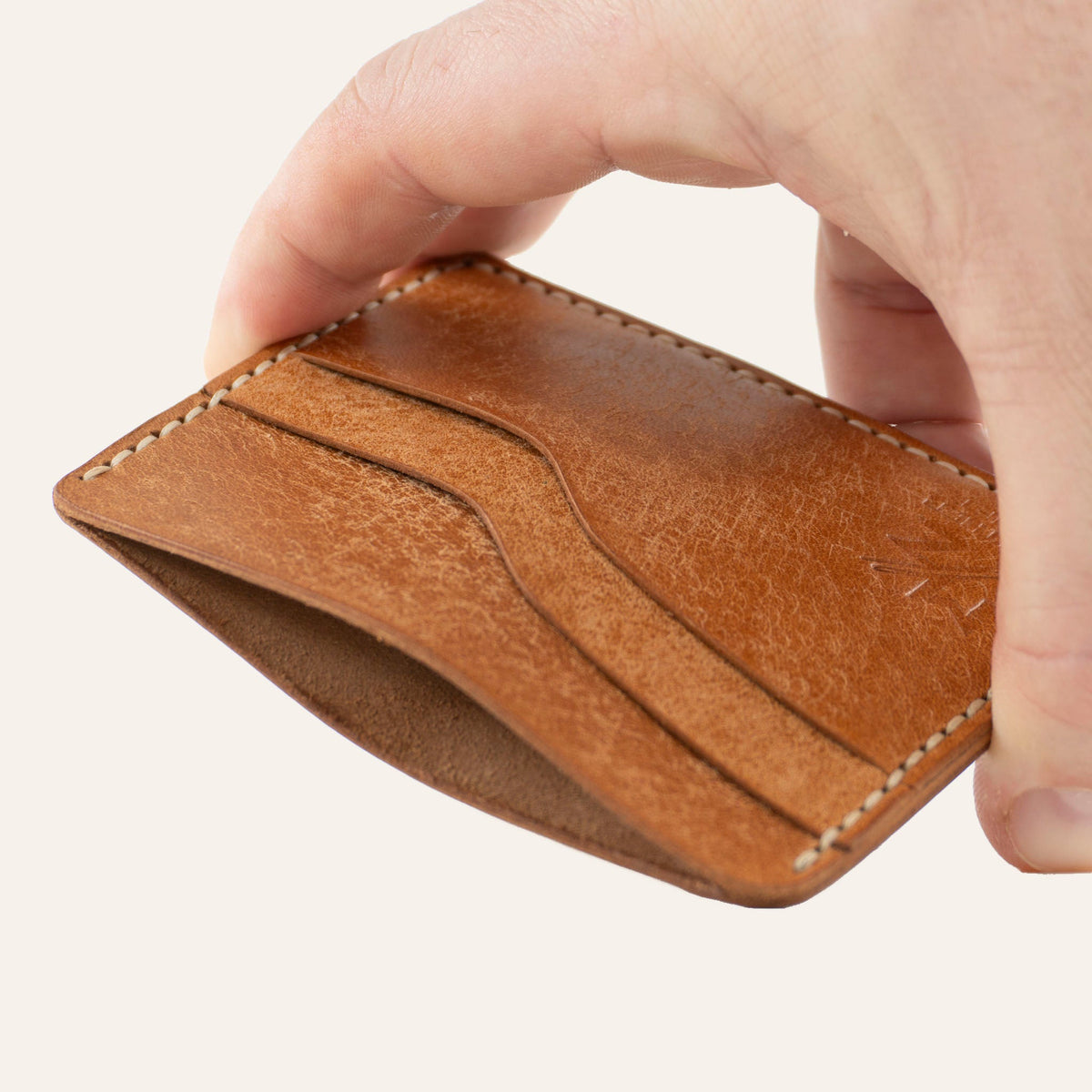 MZ Leather Craft yatay minimalist natürel Pueblo deri kartlık, el ile tutulan hafif açılı boş ön görünüm, kıvrımlı kart yuvaları ve açık gri saraç dikişi detayları
