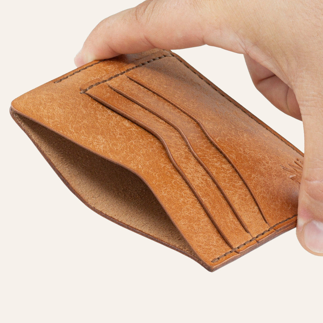 MZ Leather Craft natürel Pueblo deri ters cüzdan, el ile tutulan hafif açılı boş görünüm, ana bölmeyi ve kahverengi saraç dikişi detaylarını gösteren açı