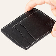 MZ Leather Craft dikey minimalist siyah Pueblo deri kartlık, el ile tutulan hafif açılı boş ön görünüm, kıvrımlı kart yuvaları ve gri saraç dikişi detayları