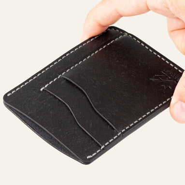 MZ Leather Craft dikey minimalist siyah Pueblo deri kartlık, el ile tutulan hafif açılı boş ön görünüm, kıvrımlı kart yuvaları ve gri saraç dikişi detayları