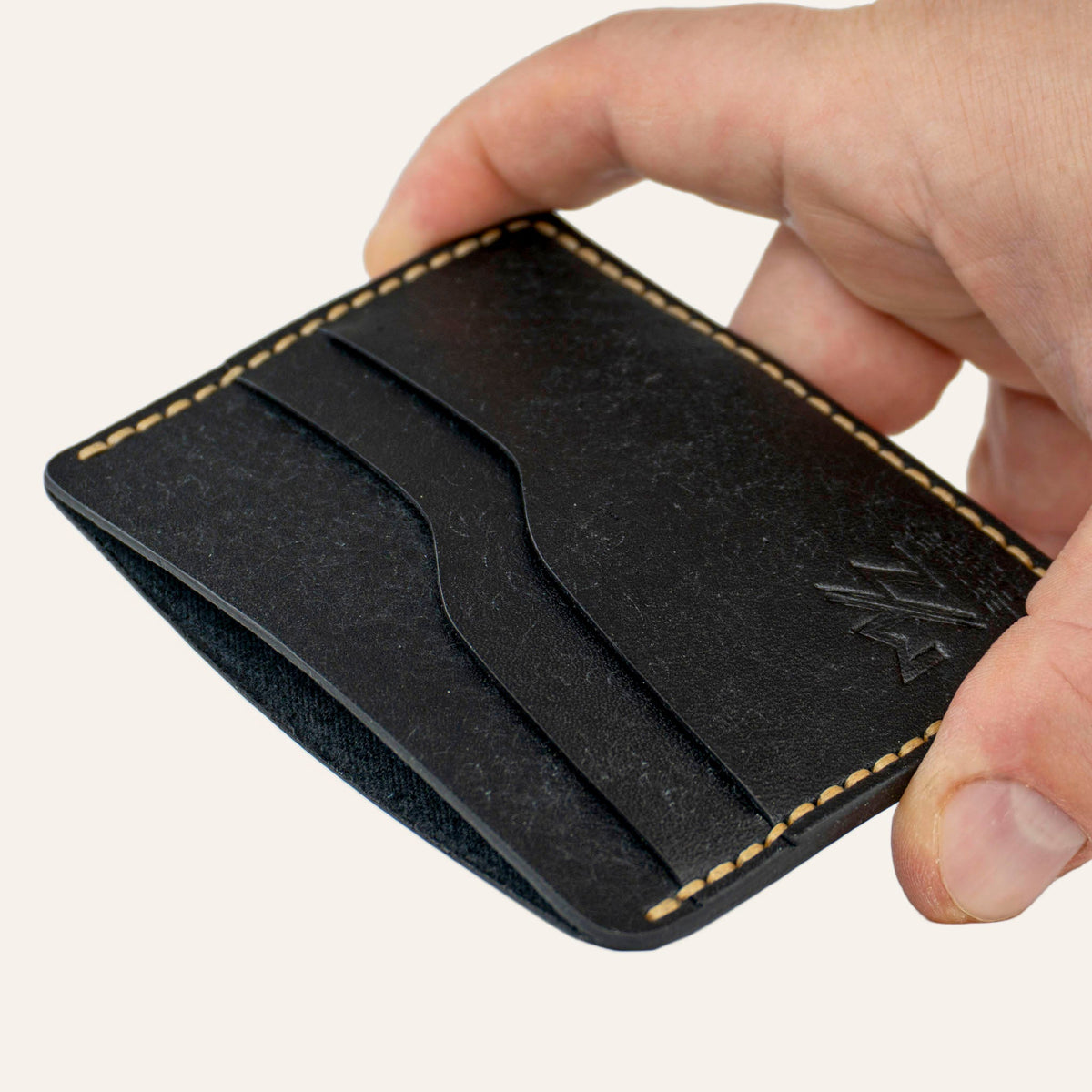 MZ Leather Craft yatay minimalist siyah Pueblo deri kartlık, el ile tutulan hafif açılı boş ön görünüm, kıvrımlı kart yuvaları ve sarı saraç dikişi detayları